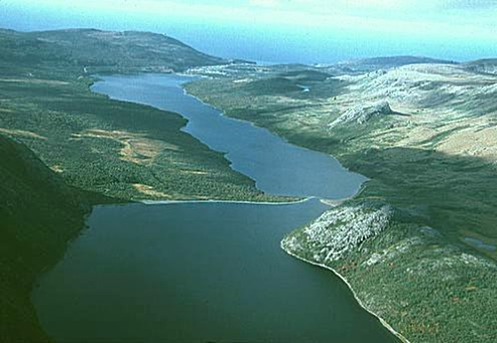 Figure 28: Gros Morne National Park, Newfoundland and Labrador - This photograph shows a wide u-shape valley covered by trees, grass and bare rock. In the middle of the valley, from the bottom to the top of the photograph, there is a river that flows into the ocean located at the top of the photograph.